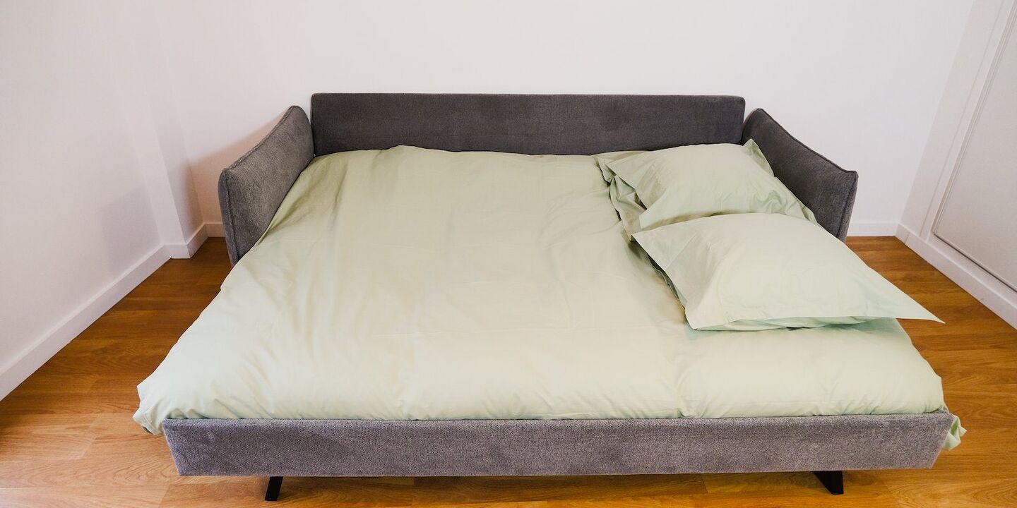 Canapé clic-clac gris déplié en lit double, garni de linge vert sauge