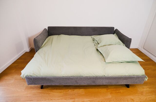 Canapé clic-clac gris déplié en lit double, garni de linge vert sauge