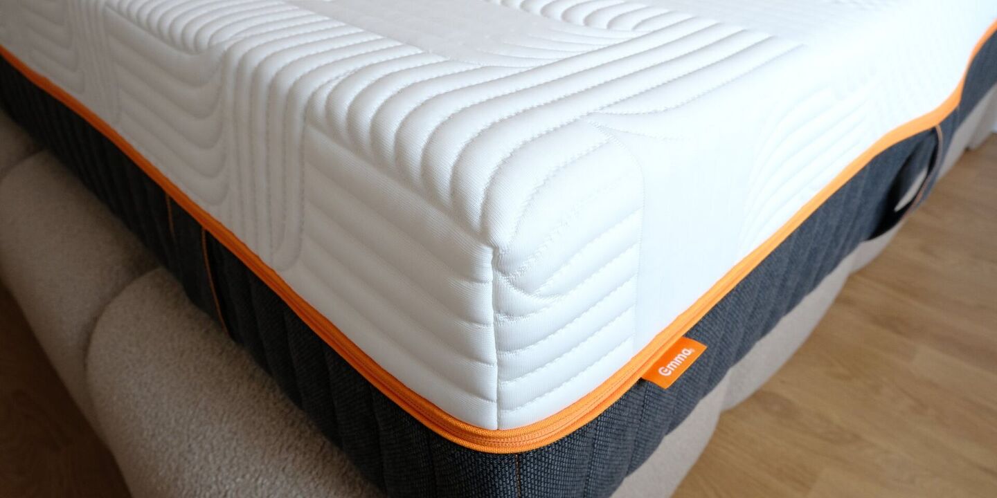 Matelas blanc à liseré orange posé sur un lit, gros plan sur l'angle