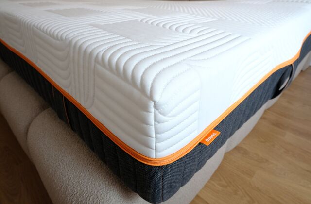Matelas blanc à liseré orange posé sur un lit, gros plan sur l'angle