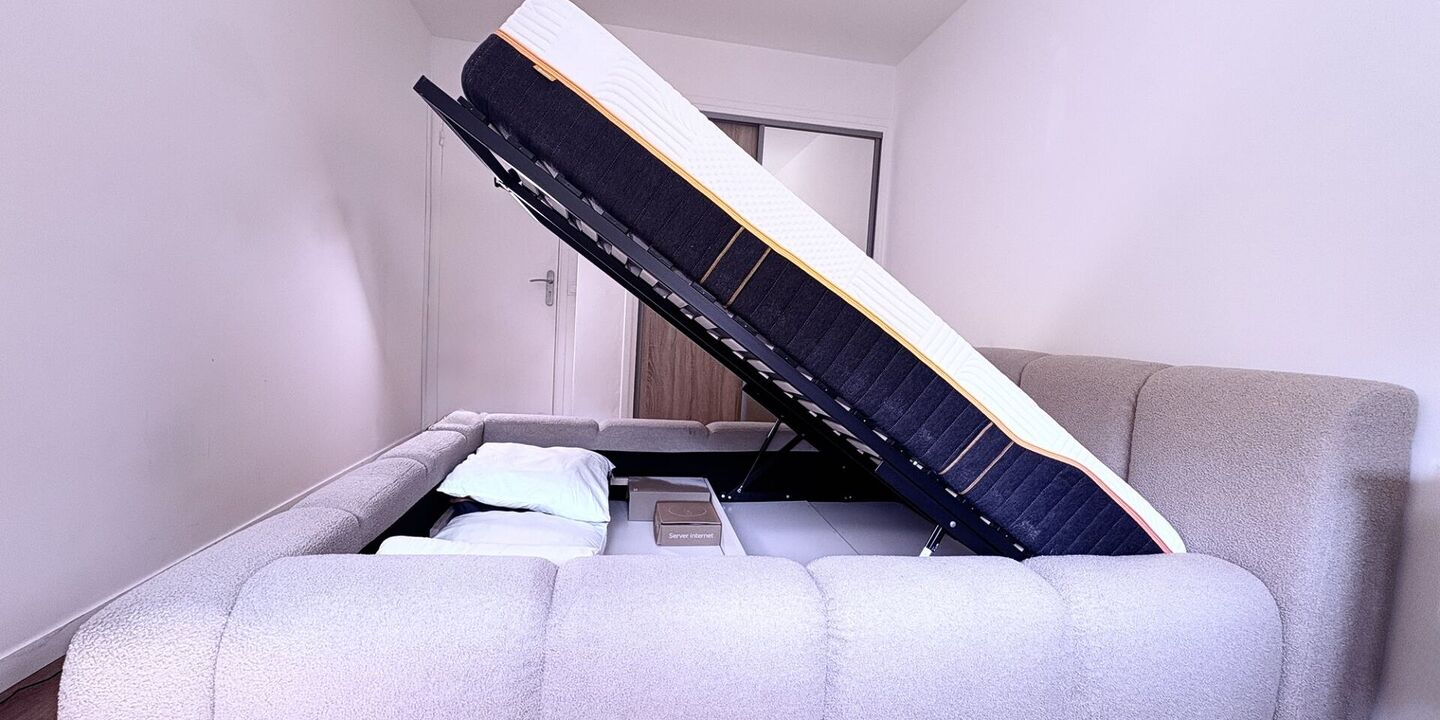 Lit coffre en tissu bouclette ouvert, le sommier relevé sur l'espace de rangement
