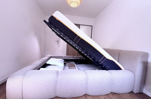 Lit coffre en tissu bouclette ouvert, le sommier relevé sur l'espace de rangement