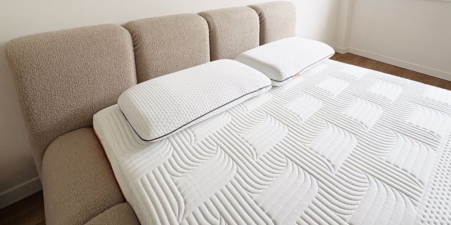 Deux oreillers en mousse posés sur un matelas blanc, devant une tête de lit bouclette