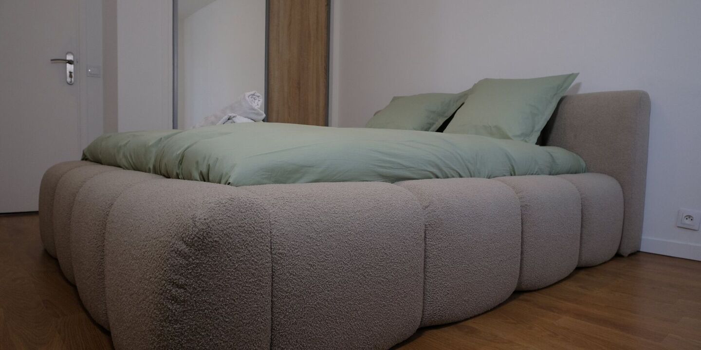 Lit en tissu bouclette avec linge vert sauge, vu de côté dans une chambre