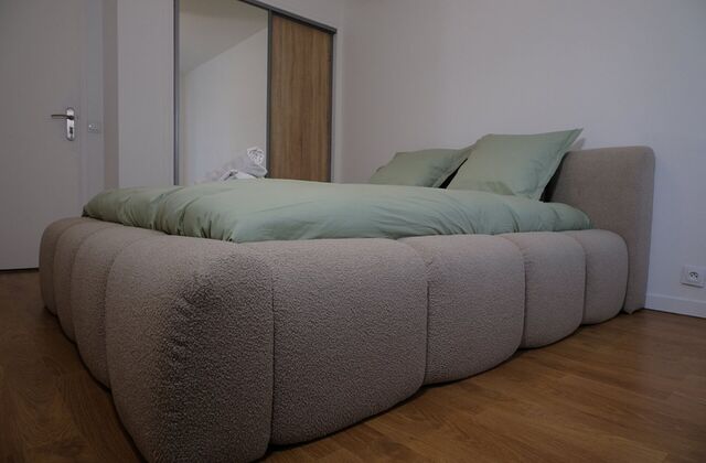 Lit en tissu bouclette avec linge vert sauge, vu de côté dans une chambre