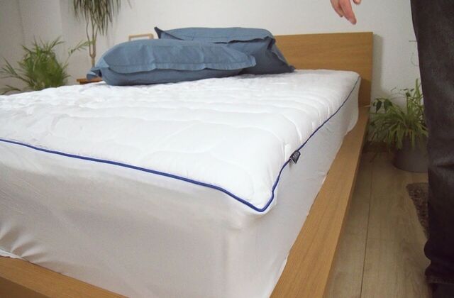 Protège-matelas blanc sur un lit en bois avec des oreillers bleus