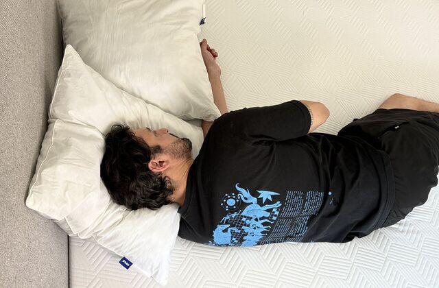 Homme couché sur le côté, de dos, entre deux oreillers