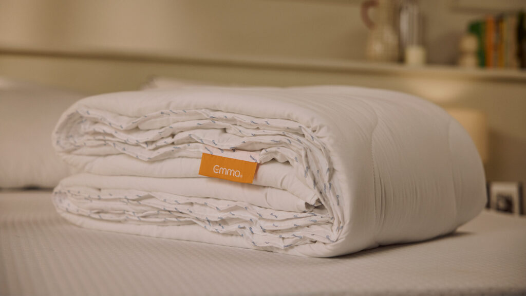 Couette Emma pliée sur un lit, étiquette orange de la marque visible