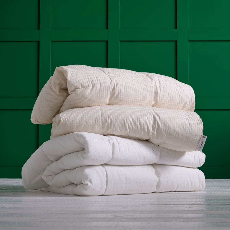Deux couettes IKEA FJÄLLHAVRE pliées l'une sur l'autre devant un mur vert