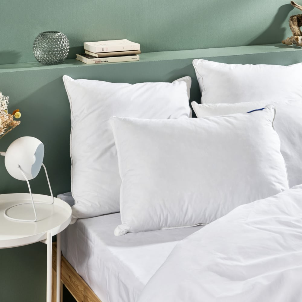 Oreillers Bleu Câlin posés sur un lit dans une chambre aux murs verts