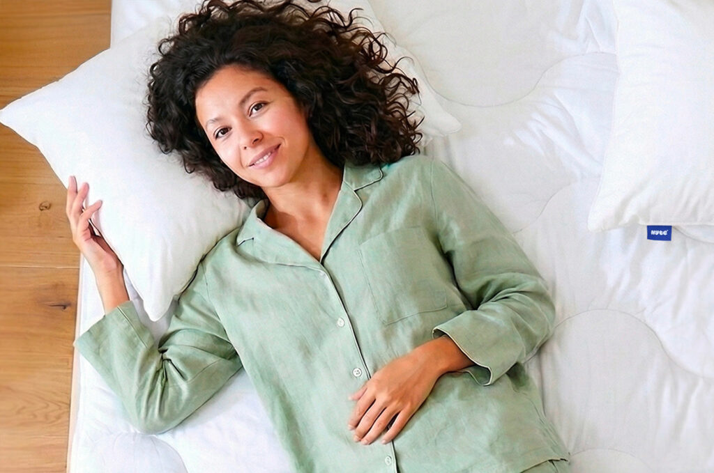 Femme allongée sur le surmatelas Nyte Duvy matelassé, lit blanc