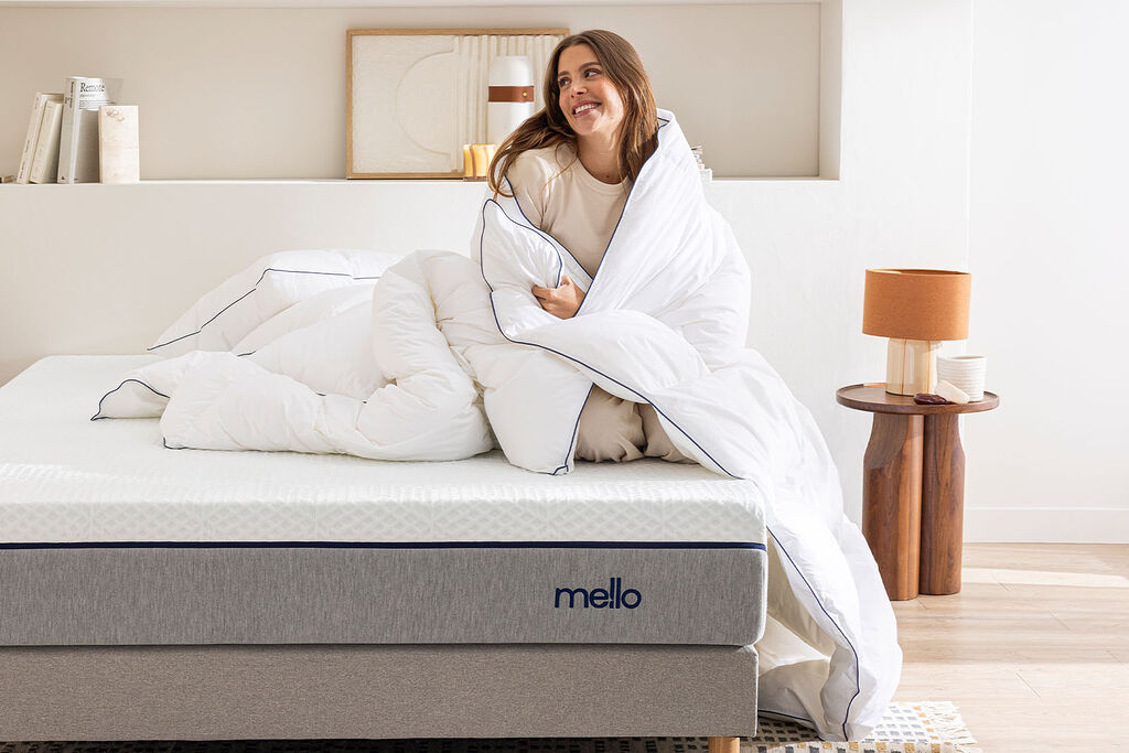 Femme enveloppée dans la couette coton Mello, assise sur un lit