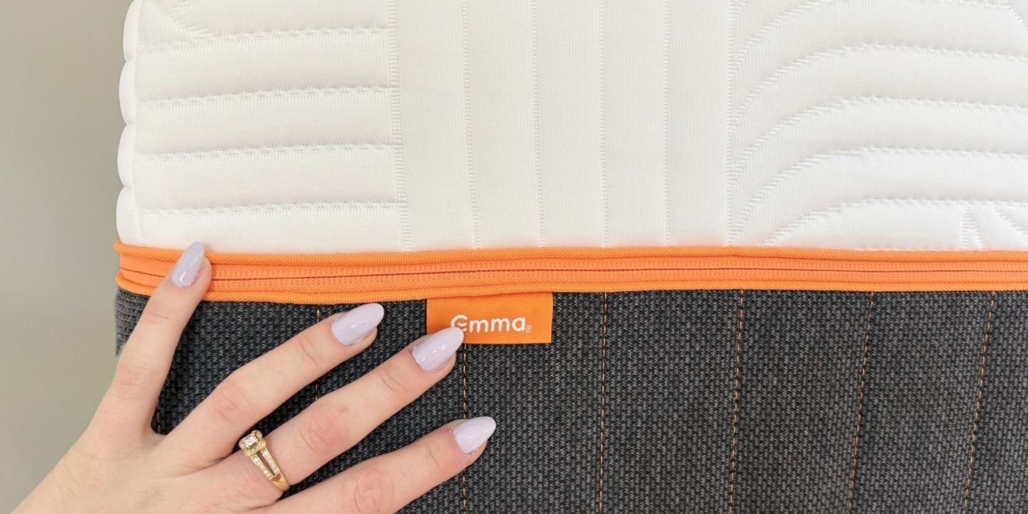 Main posée sur le flanc d’un matelas Emma, fermeture éclair orange et étiquette Emma