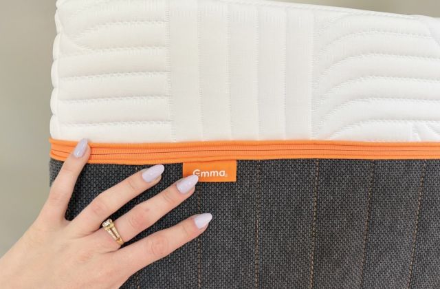 Main posée sur le flanc d’un matelas Emma, fermeture éclair orange et étiquette Emma