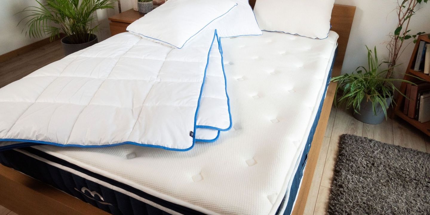 Matelas, couette et oreillers blancs sur un lit en bois dans une chambre lumineuse avec des plantes