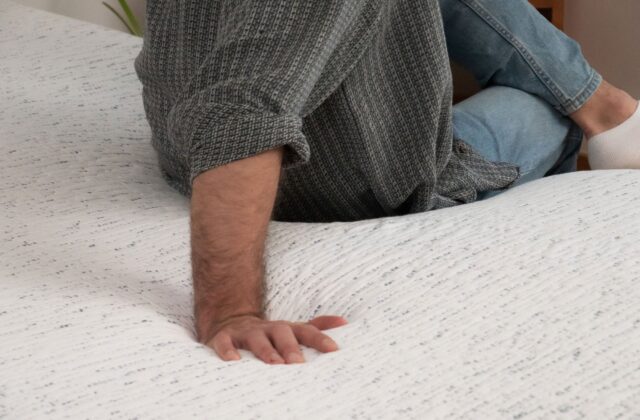 Main posée à plat sur un surmatelas, homme assis sur le lit