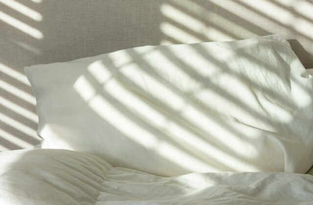Oreiller rectangulaire blanc dans sa taie, posé sur un lit sous la lumière du matin