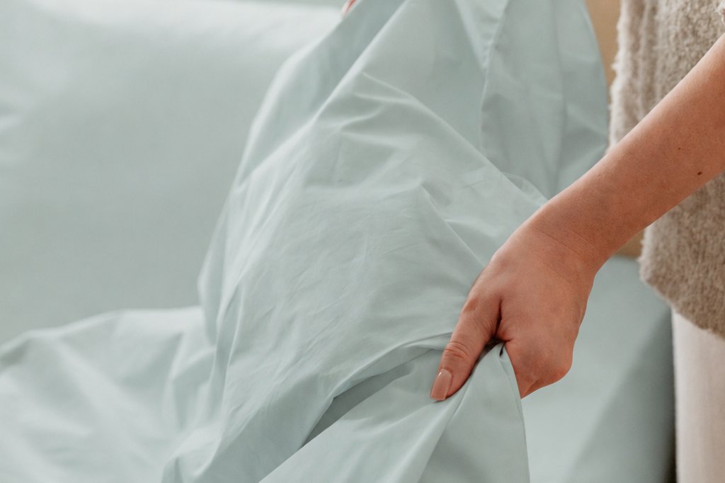 Mains ajustant la housse de couette Morphea en percale lavée sur le lit