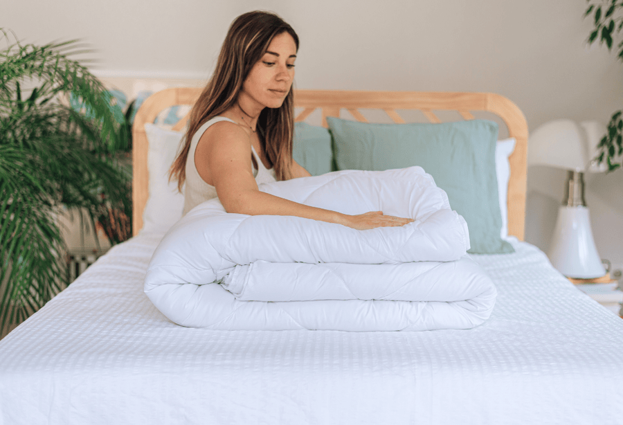 Femme posant la main sur la couette 4 saisons Slome pliée sur un lit