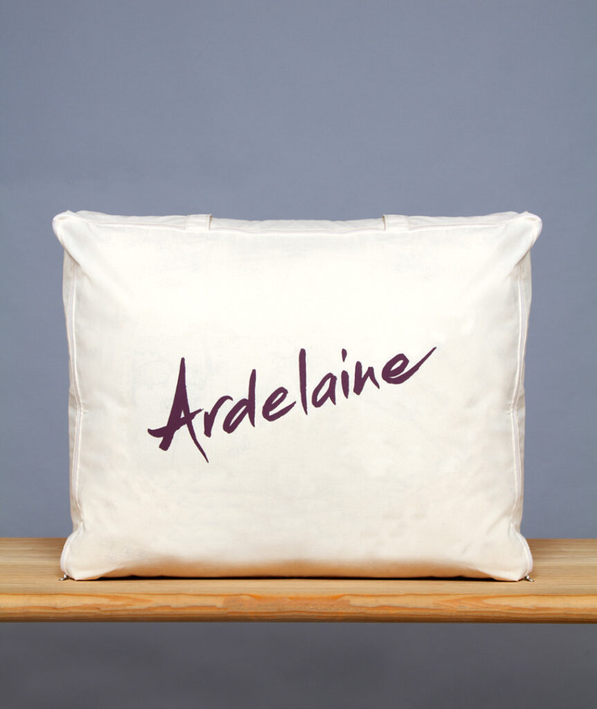 Surmatelas Ardelaine rangé dans sa housse en coton écru imprimée du logo Ardelaine