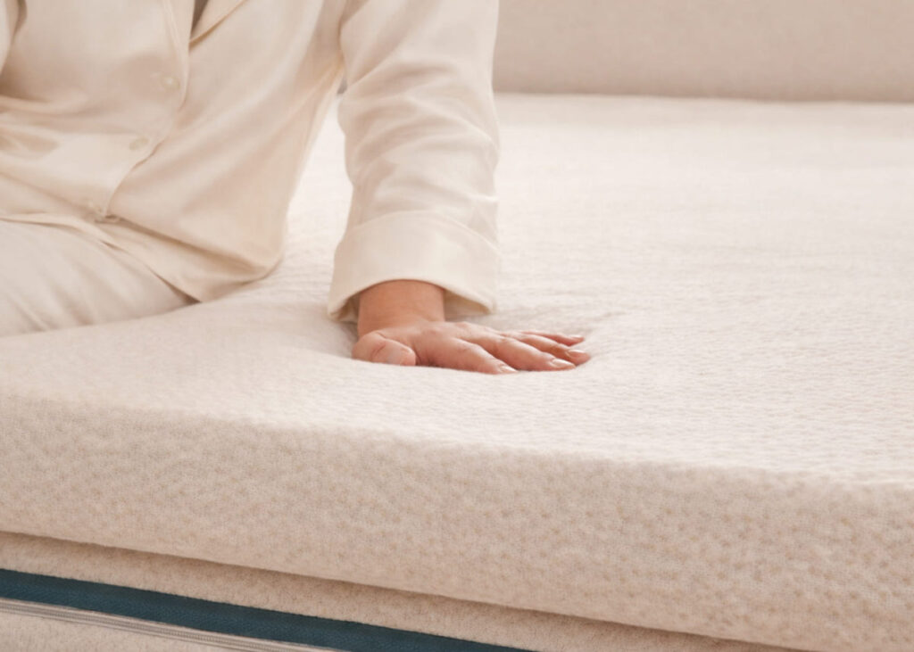 Main appuyée sur le surmatelas Kipli en latex naturel, accueil moelleux