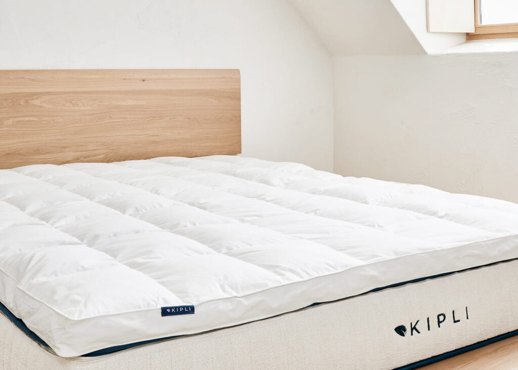 Surmatelas Kipli en plumes et duvet sur un grand lit, vue de trois quarts