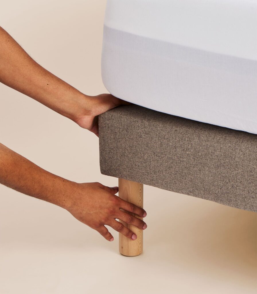 Tediber Sommier tapissier gris avec un matelas, mains ajustant le drap housse