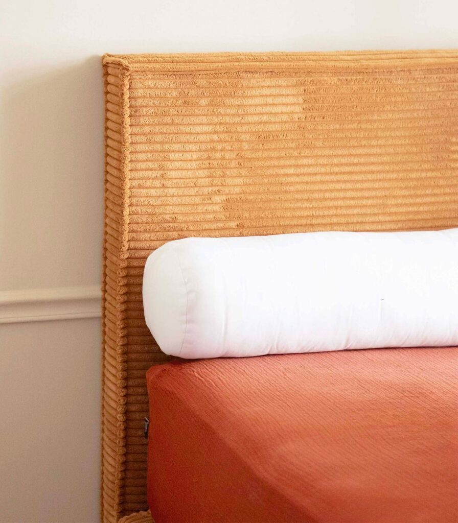 Traversin Tediber calé contre une tête de lit en velours côtelé