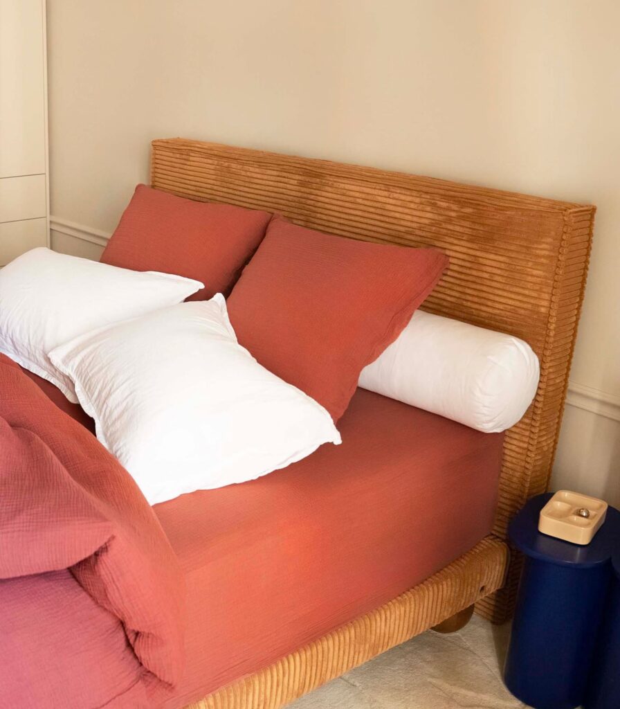 Traversin Tediber posé contre une tête de lit en velours côtelé, avec oreillers et linge terracotta